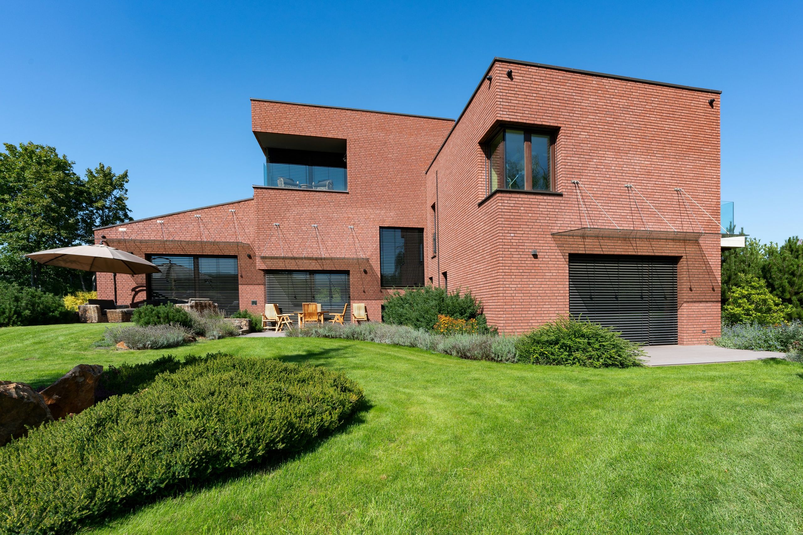 A two-storey house in red brick with deep-set windows, a terrace and a planted garden
