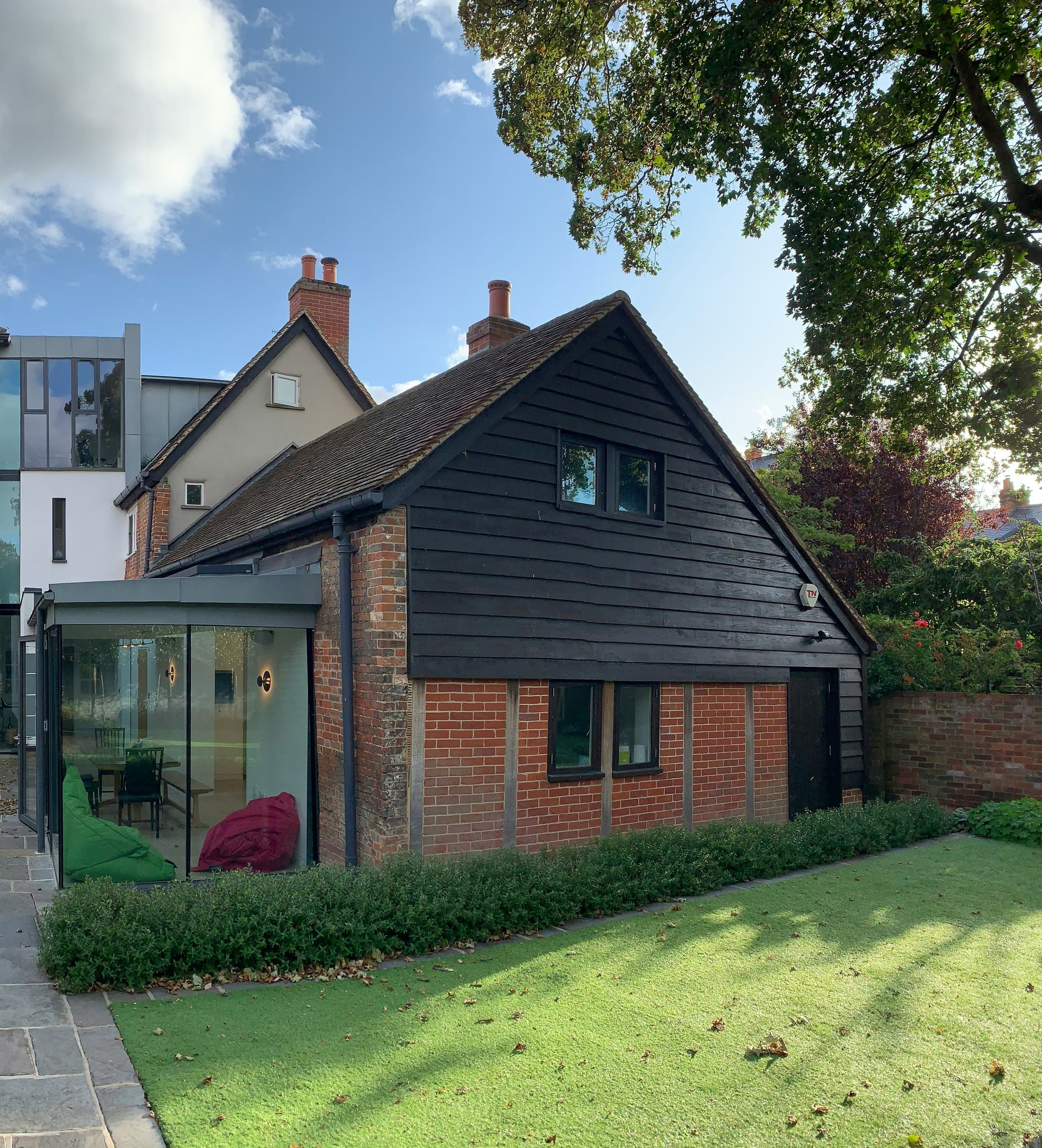 A glazed link joining an older brick house to a black weatherboard outbuilding